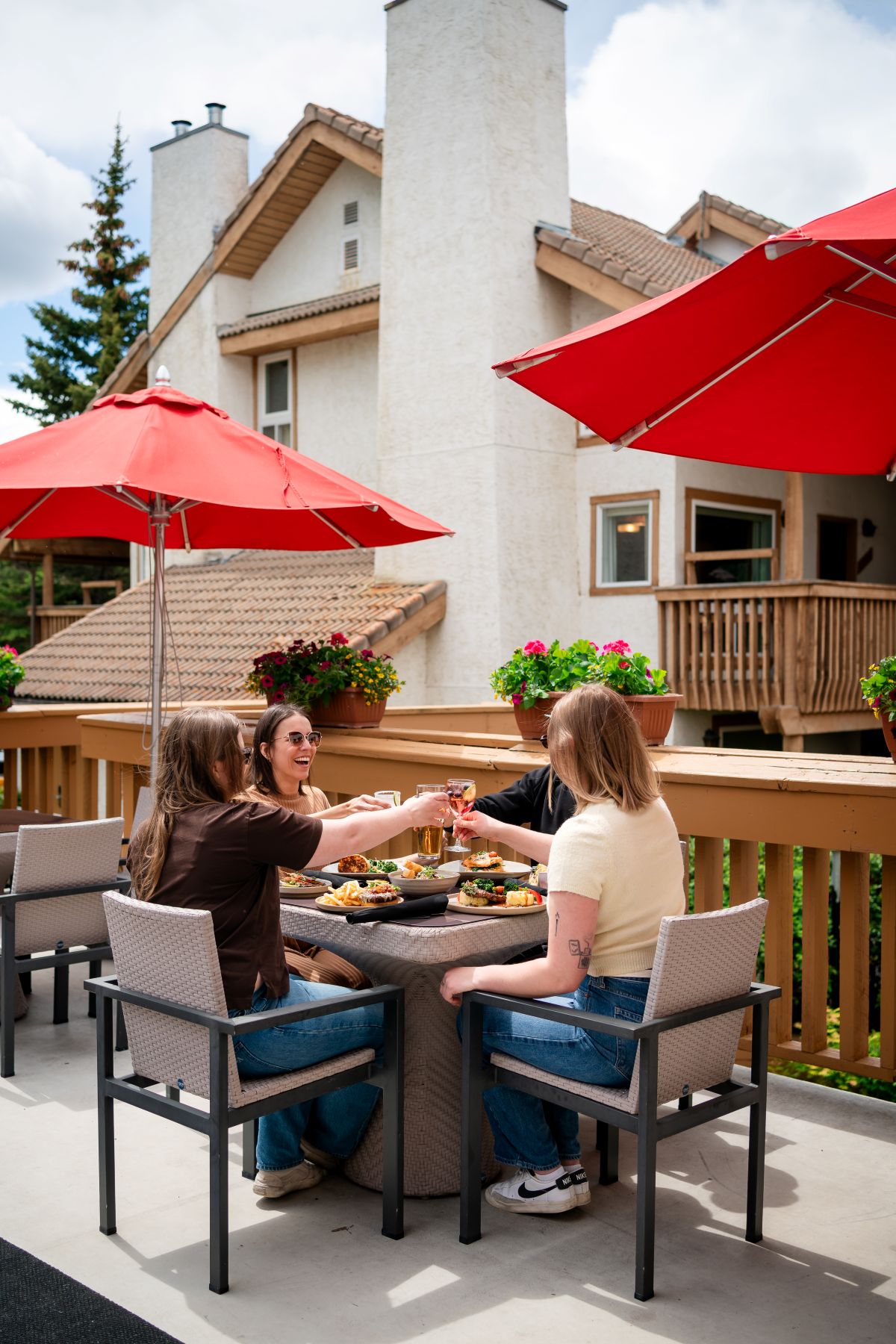 Four friends having drinks and food on a patio with red umbrellas