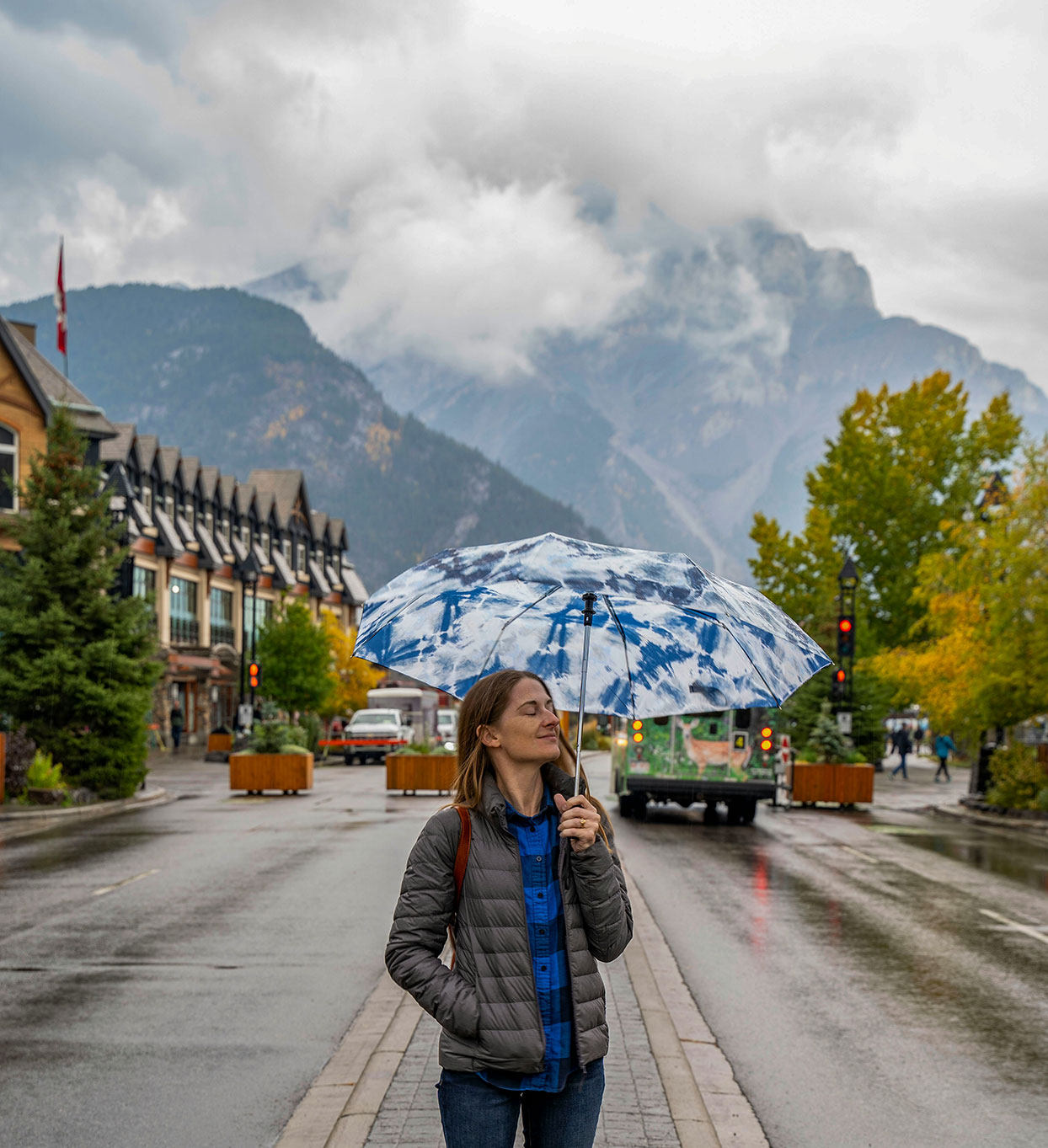 Woman standing on Banff Avenue in the rain with mountain backdrop